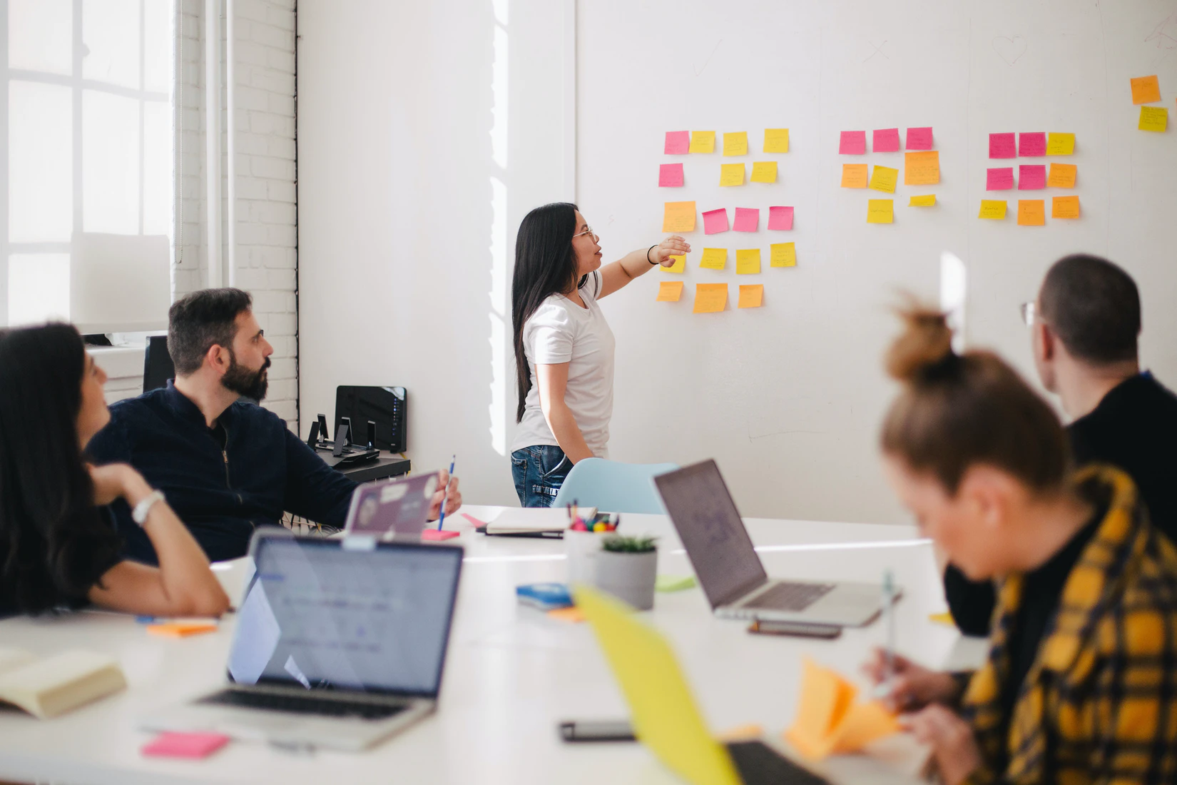 personas en una mesa reunidas con un tablero de fondo con post-it de colores